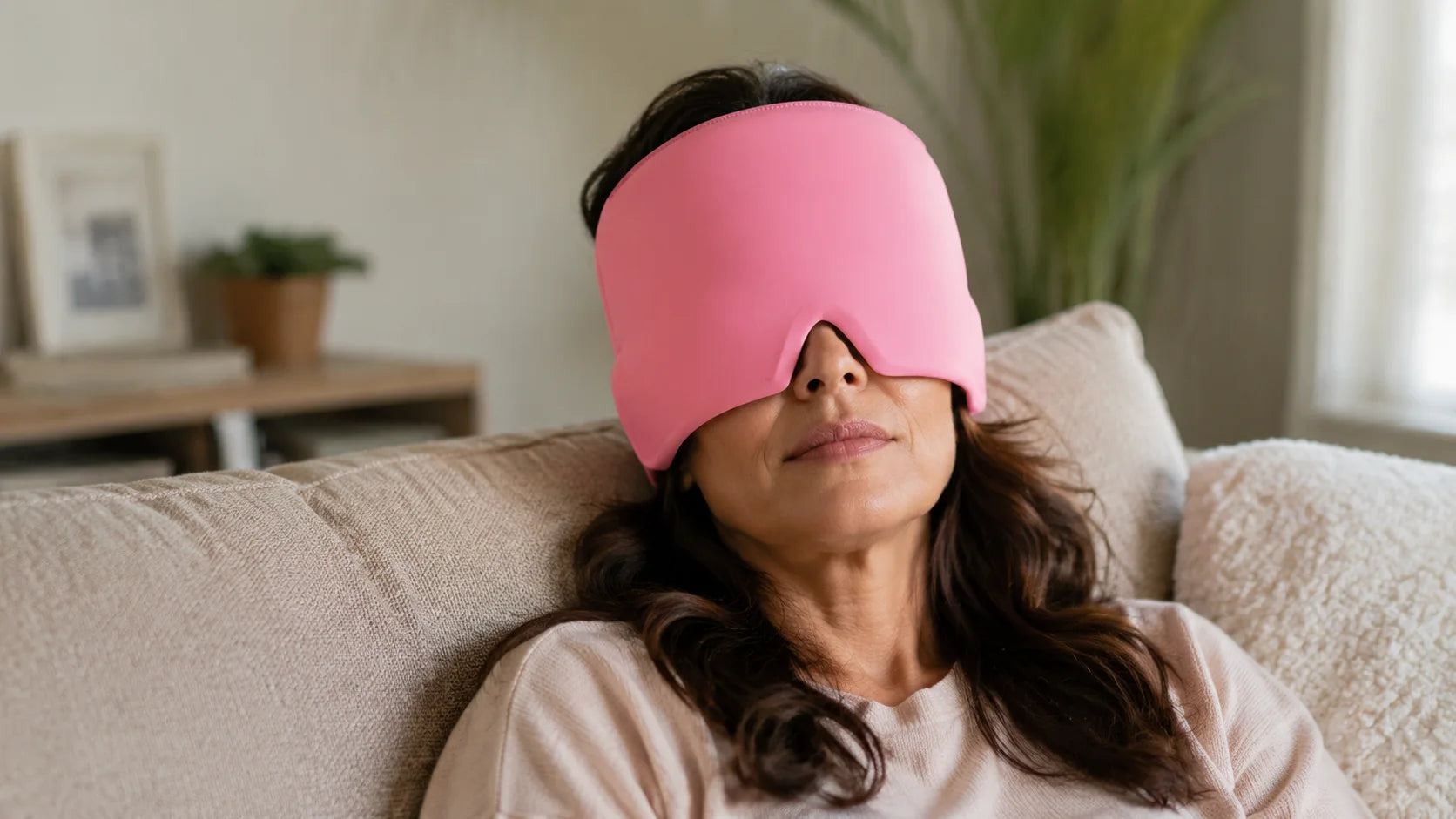 A woman resting on a sofa with a pink NuraCool cap positioned over her eyes